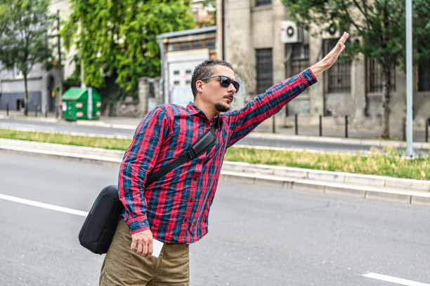 一个穿着格子衬衫的商人正站在街上挥手叫出租车。图片下载