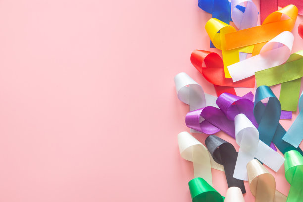 彩色丝带蝴蝶结上柔和的粉红色背景在俯视图平lay与文本的复制空间。世界癌症日活动理念2月4日，癌症意识。国家癌症生存日。图片下载