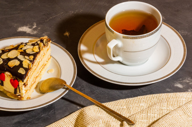 静物层次的自制海绵蛋糕和一杯红茶在一个白色的盘子，和亚麻餐巾，黑色的背景，强光，照片在一个低的关键。图片下载