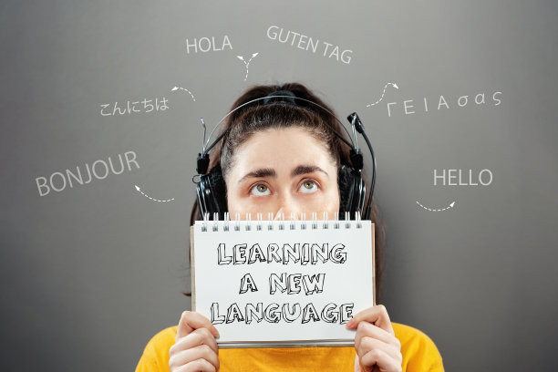 一名年轻女子的肖像，戴着耳机，拿着笔记本，抬头看着外国问候，遮住了她的一半脸。灰色的背景。学习外语的概念图片下载