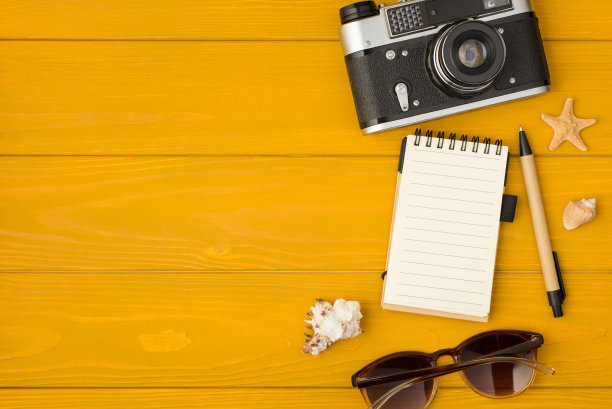 头顶照片的相机、记事本、钢笔、贝壳、海星和太阳眼镜孤立在黄色的木制背景图片下载