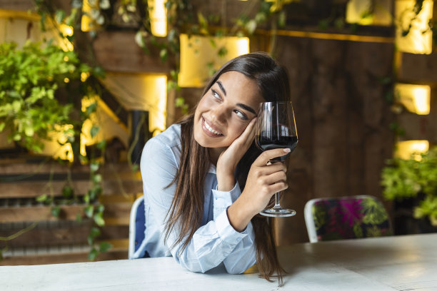 坐在餐厅里品酒的美女。可爱的年轻女子坐在咖啡馆拿着酒杯喝着葡萄酒。一个美丽的品酒女游客的肖像。图片下载
