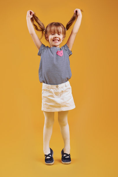可爱的小女孩，穿着休闲装，在黄色背景下的演播室里玩耍图片下载