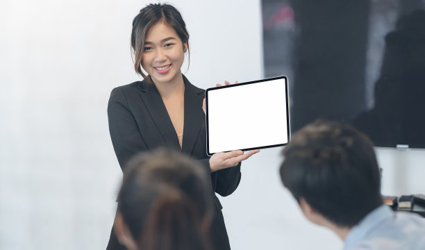年轻美丽的亚洲女商人展示数字平板电脑屏幕和展示商业计划，而站在会议室与她的业务团队。图片下载