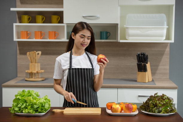 女人烹饪和切苹果在木砧板上准备健康的食物，手握刀和水果切片在厨房的桌子上图片下载