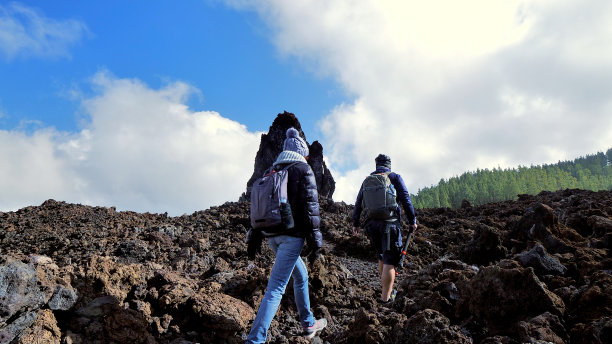 在特内里费(加那利群岛)的埃尔奇耶罗火山，两个徒步旅行者正走在熔岩流上，朝着一块高高的火山岩走去。图片下载