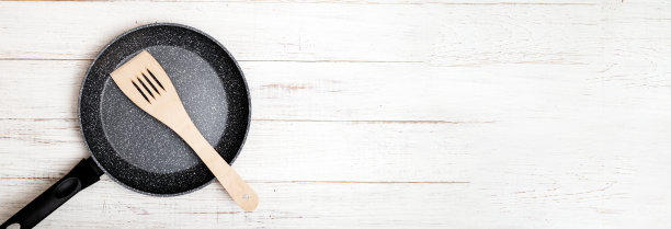 用不粘陶瓷涂层和抹刀在白色木制背景上煎锅。烹饪不粘或油。横幅图片下载