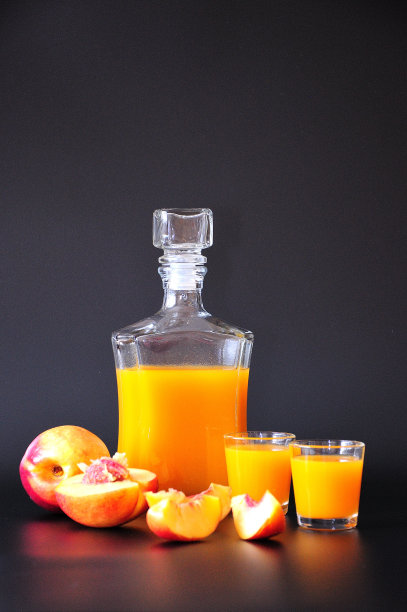 两个玻璃杯和一瓶桃子利口酒旁边的新鲜水果在一个黑色的背景。图片下载