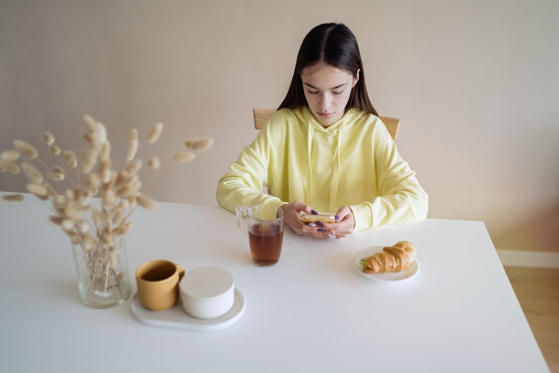 一名少女在厨房边吃早餐边玩智能手机图片下载