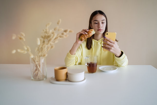 一名少女在厨房边吃早餐边玩智能手机图片下载