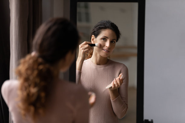 迷人的拉丁女人看着镜子，握着刷子，抹着粉图片下载