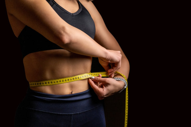 一位年轻的运动员正在用卷尺测量自己的腰围。图片下载