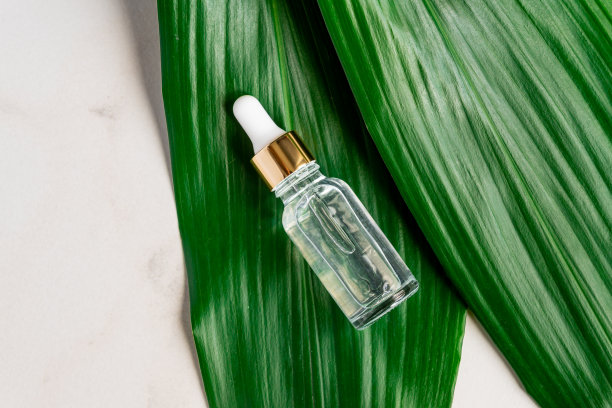 大理石桌上放着一瓶血清，背景是绿色的棕榈叶。滴管瓶与天然有机化妆品。SPA、护肤、身体护理理念。图片下载