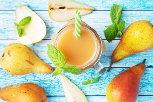 玻璃杯里的天然梨汁。多汁的成熟的梨和薄荷叶。俯视图亮蓝色背景。图片下载