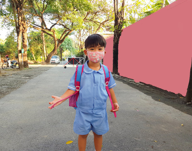 一个3岁的亚洲男孩穿着校服，戴着面具在学校前微笑。准备好学习。新师范学校。学生戴口罩预防新冠肺炎疫情爆发。快乐的孩子。图片下载