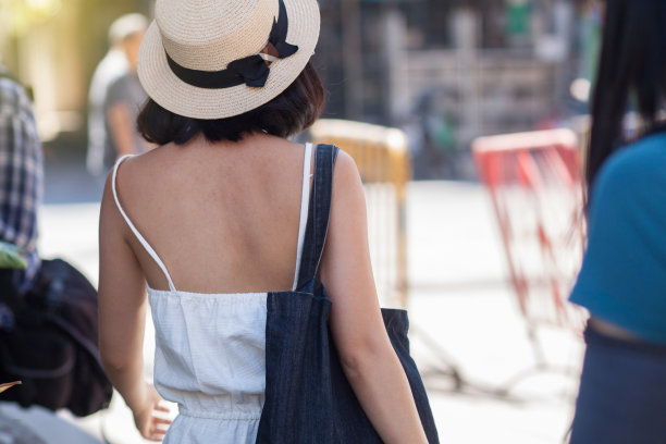 这名女游客身穿白色连衣裙，背着一个包，戴着一顶帽子，走在新鲜市场的人行道上。图片下载