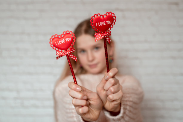 可爱的金发女孩拿着印有红布爱心和“我爱你”字样的棍子图片下载