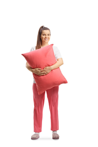 一位穿着睡衣抱着枕头微笑的年轻女性的全长肖像图片下载