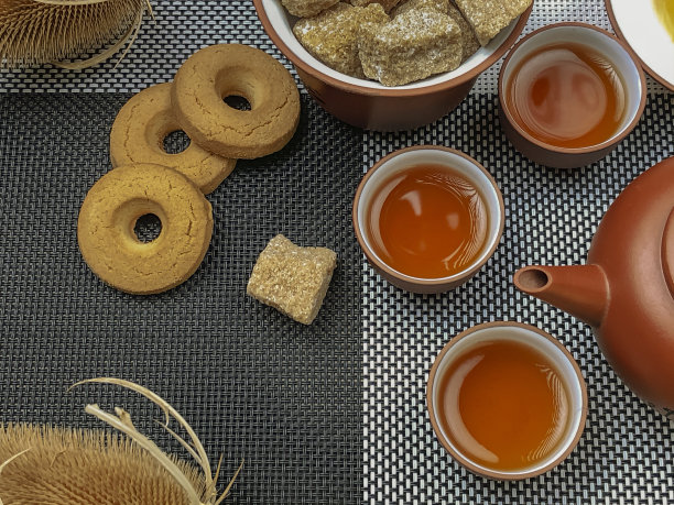 中国棕色茶具一套茶壶和三个杯子，饼干和棕糖在竹席上。特写照片，从上面看。图片下载