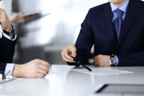 商务人士在会议或谈判中讨论合同，坐在一起，背景是一个不认识的女人，特写。一群不知名的商人在一个现代化的办公室里。团队合作、伙伴关系的概念图片下载