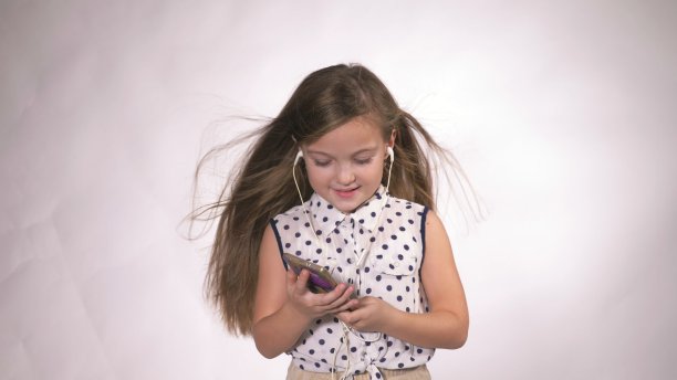 孩子戴着耳机在演播室里跳舞。女孩用智能手机听音乐。美丽可爱快乐的小女孩听音乐。图片下载