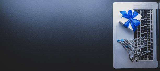 网上购物。笔记本电脑，购物车和白色礼物与蓝色丝带在黑暗的背景。易电子商务网站商店。客户体验的概念。图片下载