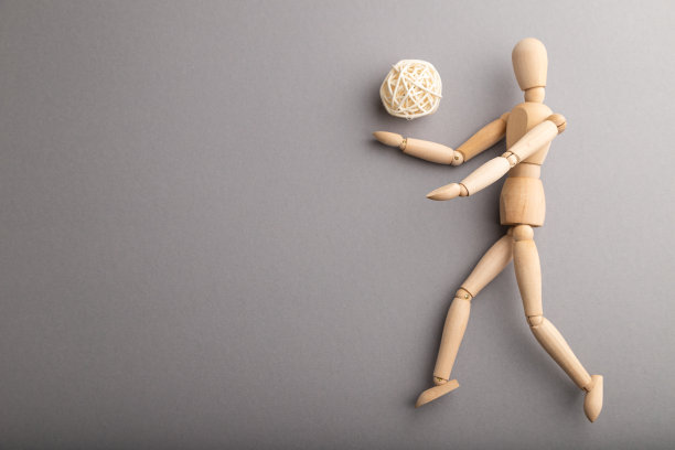 木制的人体模型在灰色柔和的背景上踢足球。复制空间，隔离，运动概念。图片下载