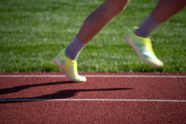 穿着黄色运动鞋的跑步者的脚在田径跑道上赛跑图片下载