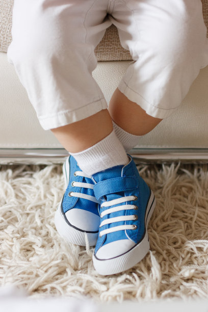 俯视图上的小男孩坐在沙发上，穿着亮蓝色的运动鞋。穿运动鞋的男孩准备去散步图片下载