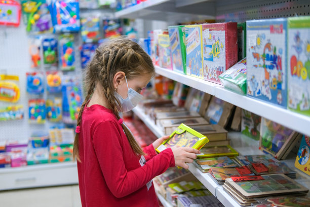 一个戴着医用口罩的孩子正在商店里挑选儿童玩具。一名女孩正在COVID-19大流行期间购物。图片下载