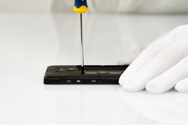 戴着白手套的手用螺丝刀拆开手机。图片下载