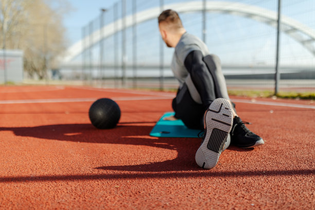 这张照片拍摄的是一个年轻人在河边跑步前伸伸腿。桥的背景。图片下载