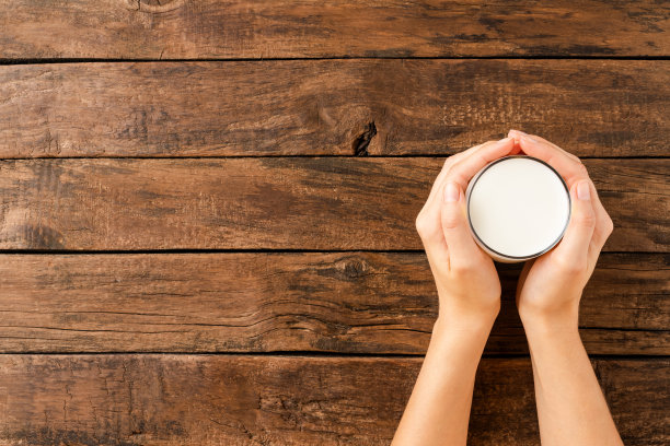 女人的手拿着一杯牛奶在带有复印空间的质朴木桌上。俯视图图片下载