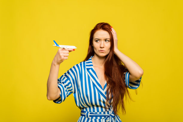 年轻美丽的红发女人在黄色背景与愤怒的脸，消极的标志，拒绝概念的飞机。这位女士因丢失行李、度假失败或航班失败而生气图片下载