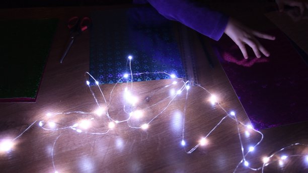 模糊的圣诞彩灯和孩子们的手触摸着闪闪发光的工艺品纸，在节日里制作工艺品图片下载