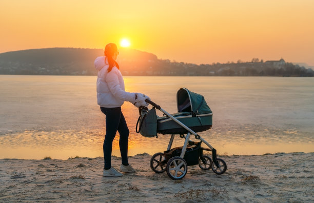 日落时分，一位年轻的母亲推着婴儿车走在冰冻的湖边。图片下载