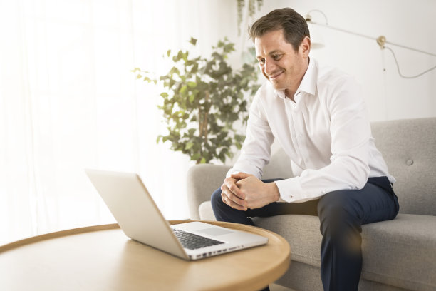 快乐微笑的年轻人看和工作在电脑笔记本电脑在家里图片下载