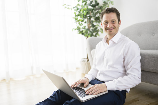 快乐微笑的年轻人看和工作在电脑笔记本电脑在家里图片下载