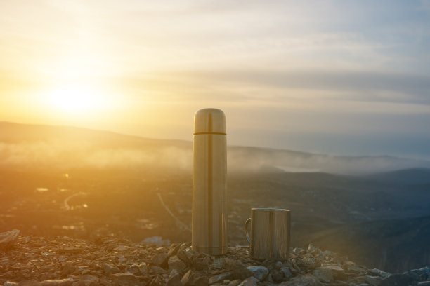 在山顶上落日的背景下，放着热水瓶和马克杯图片下载