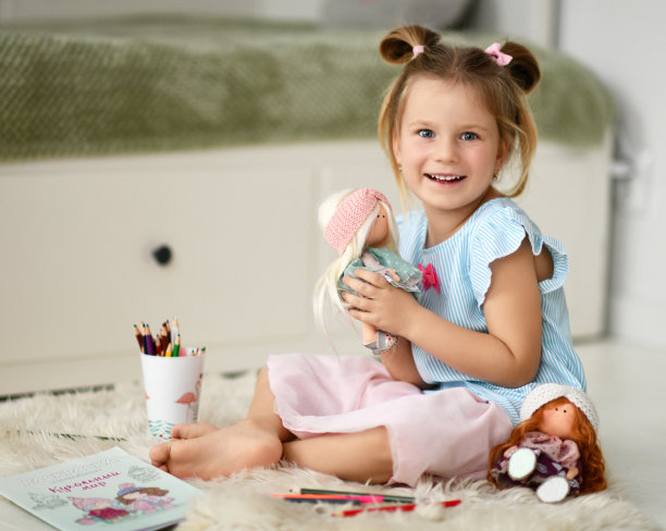 快乐的小女孩光着脚坐在家里柔软的地毯上玩娃娃，用彩色的铅笔画画图片下载