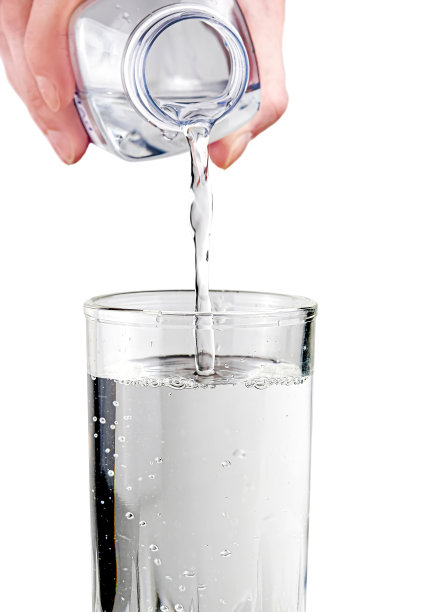 在光线充足的背景下，将瓶子里的水倒在玻璃上。天然矿泉水。图片下载