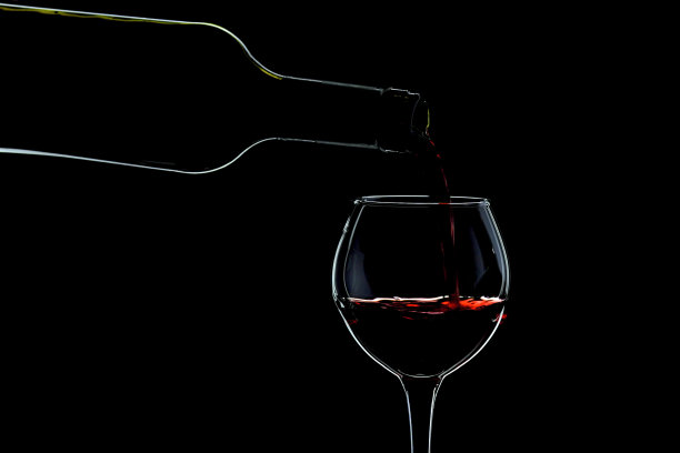 在黑色背景上，用轮廓照明从瓶子里倒酒的玻璃杯。图片下载