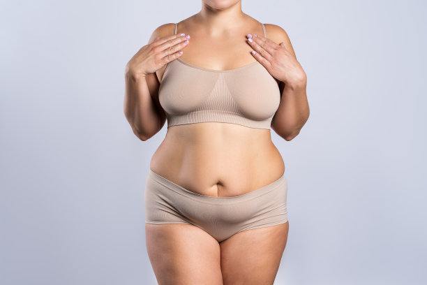 胖女人穿着米色内衣在灰色的背景下，超重的女性身体图片下载