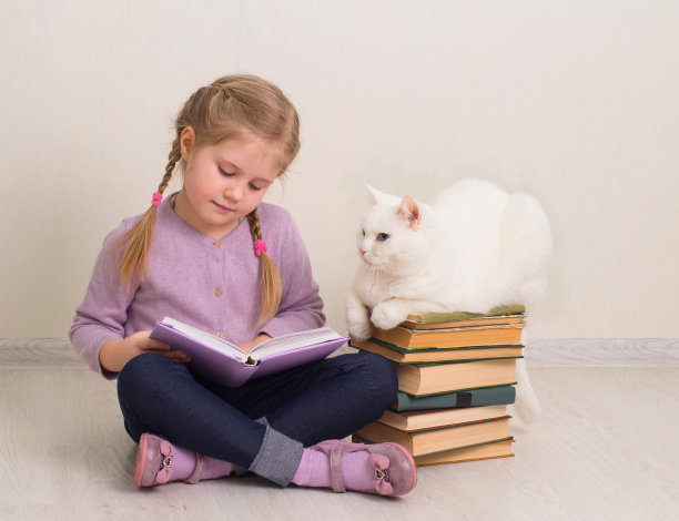 一个微笑的小女孩和她的猫坐在地板上读一本书。教育、休闲、宠物理念。图片下载