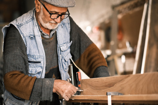 一位年长的男木匠在他的旧车间里工作。图片下载