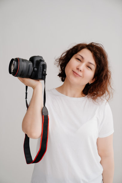 白色背景上穿着t恤的黑发女人，手里拿着照相机。图片下载