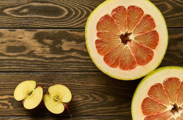 红柚子和苹果两半放在一张木桌上，有复印空间图片下载