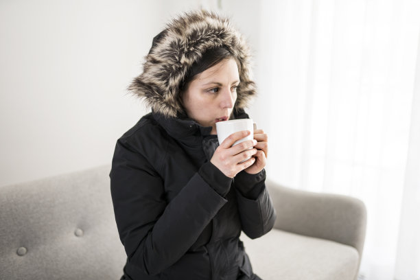 女人喝着咖啡，穿着暖和的衣服，坐在沙发上感受屋内的寒冷图片下载