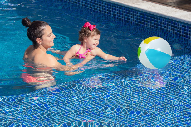 一个阳光明媚的夏日，母亲和女儿在游泳池里玩耍图片下载