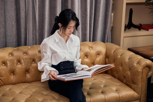 坐在沙发上看书的亚洲女人。图片下载